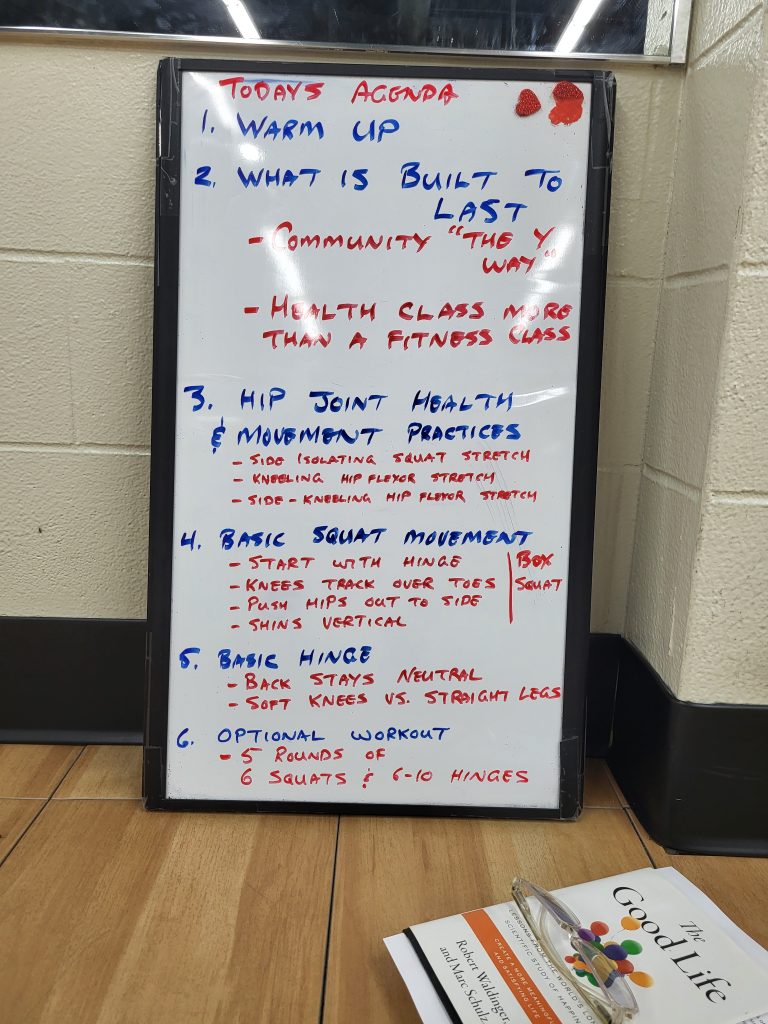Whiteboard with a handwritten agenda in red and blue marker (Today’s Agenda) listing warm-up, workout topics, and health class notes in a gym setting.